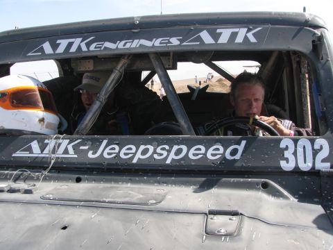 1990 Ford Bronco - driver wearing a helmet sits at the wheel of the caged ATK-Jeepspeed race vehicle numbered 302.