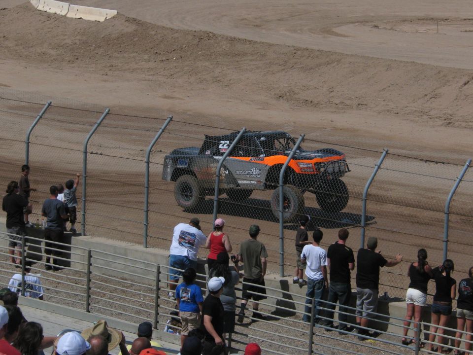 Orange and black number 22 off-road race truck on a dirt track with crowd