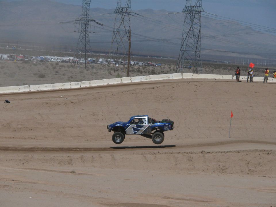 Blue and white off-road race truck jumping on a banked dirt desert track