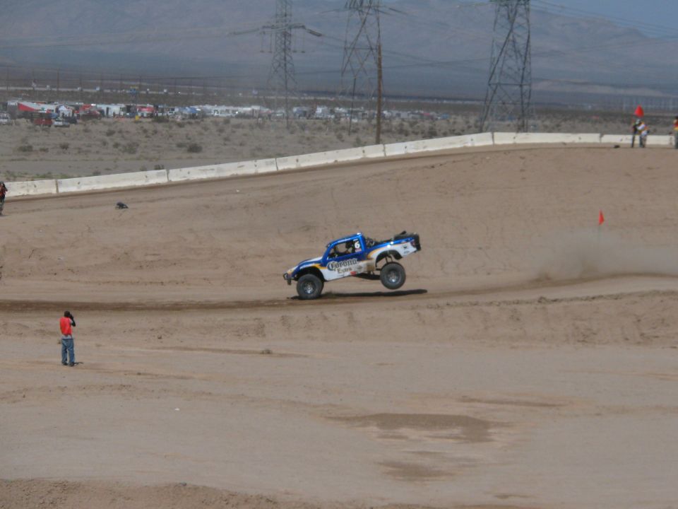 Blue and white off-road race truck cornering on a banked dirt desert track