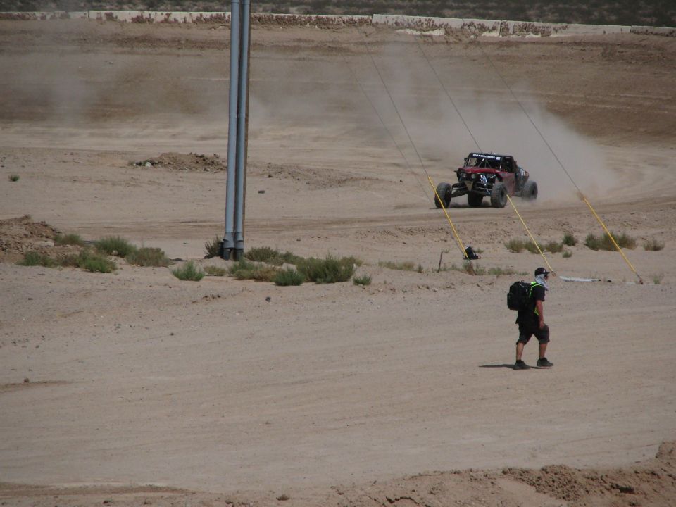 Off-road buggy kicking up dust in desert with a person walking in foreground