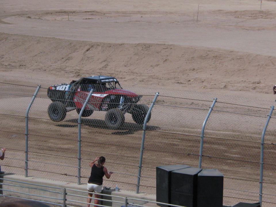 Black and red off-road race truck on dirt track behind chain-link fence