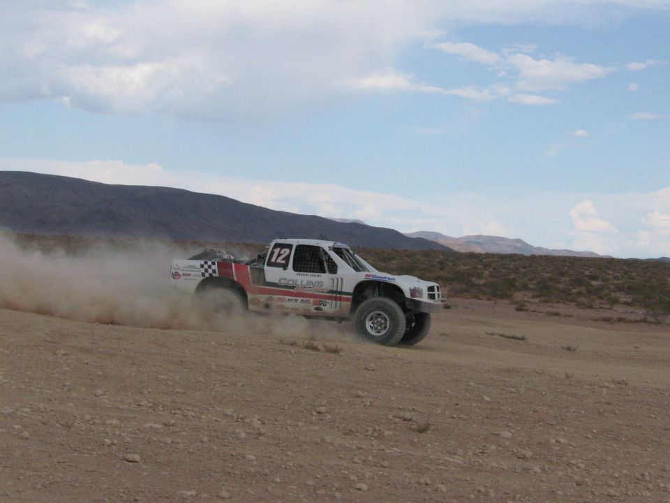 White and red off-road race truck #12 racing through dusty desert