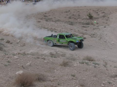 1990 Ford Bronco - green off-road race truck marked Ashcraft slides through a dusty banked turn on a desert course.