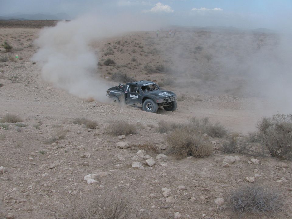 Dark off-road race truck sliding through dusty desert turn surrounded by scrub