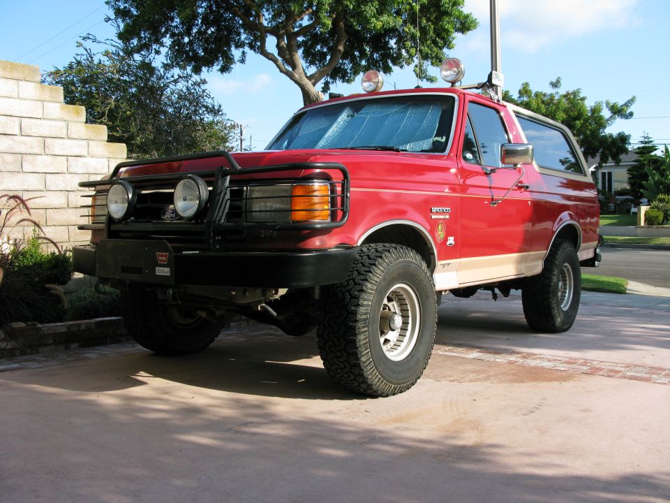 Red and tan Ford Bronco with black brush guard bumper and roof lights in driveway