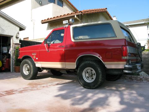 1989 Ford Bronco - Red 1989 Ford Bronco with a tan removable top is parked in a driveway.