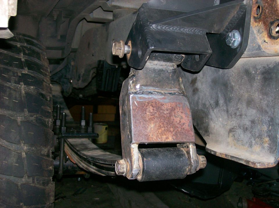Close-up of a modified leaf spring mount on a vehicle's suspension, showing custom brackets and hardware