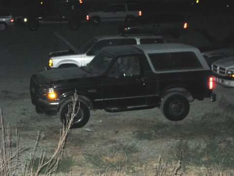 1989 Ford Bronco - A black Ford Bronco with a silver top is parked outdoors at night, with other vehicles visible in the background.