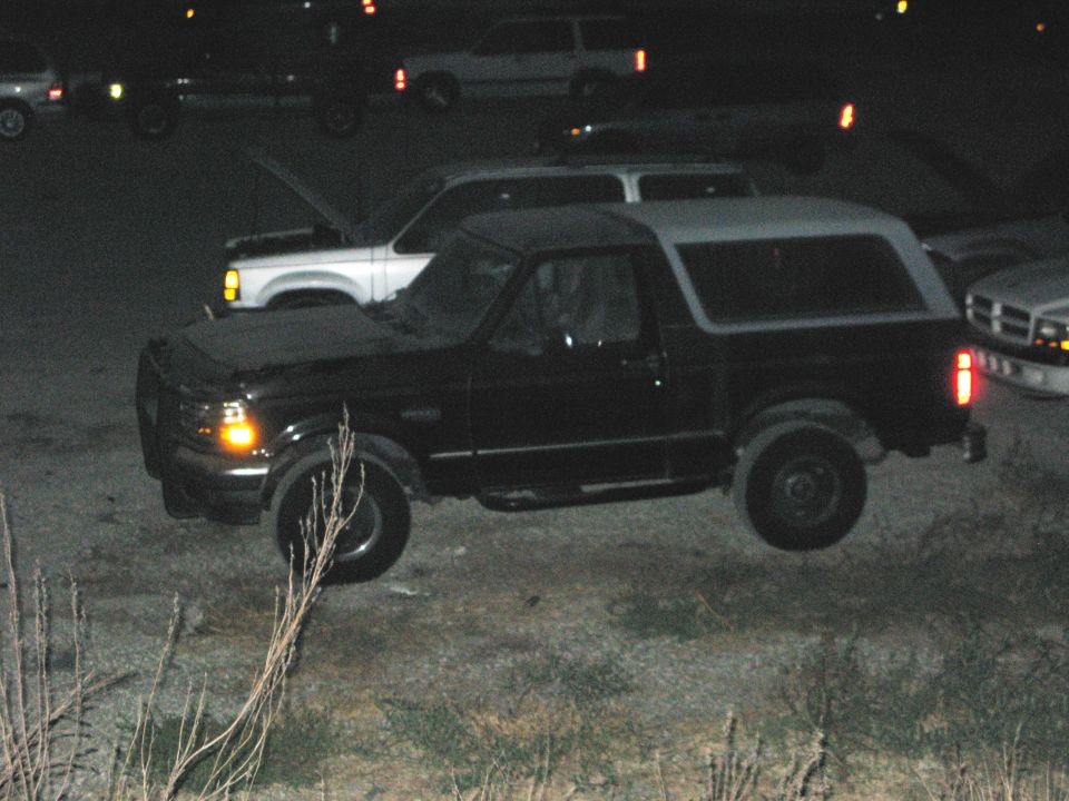 Dark Ford Bronco with light hardtop parked at night among other trucks