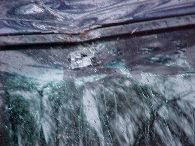 Close-up of a damaged vehicle's body panel and shattered windshield glass