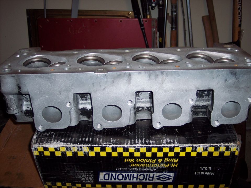 Aluminum engine cylinder head with visible ports and valve seats, resting on a Richmond Hi-Performance Ring & Pinion Set box