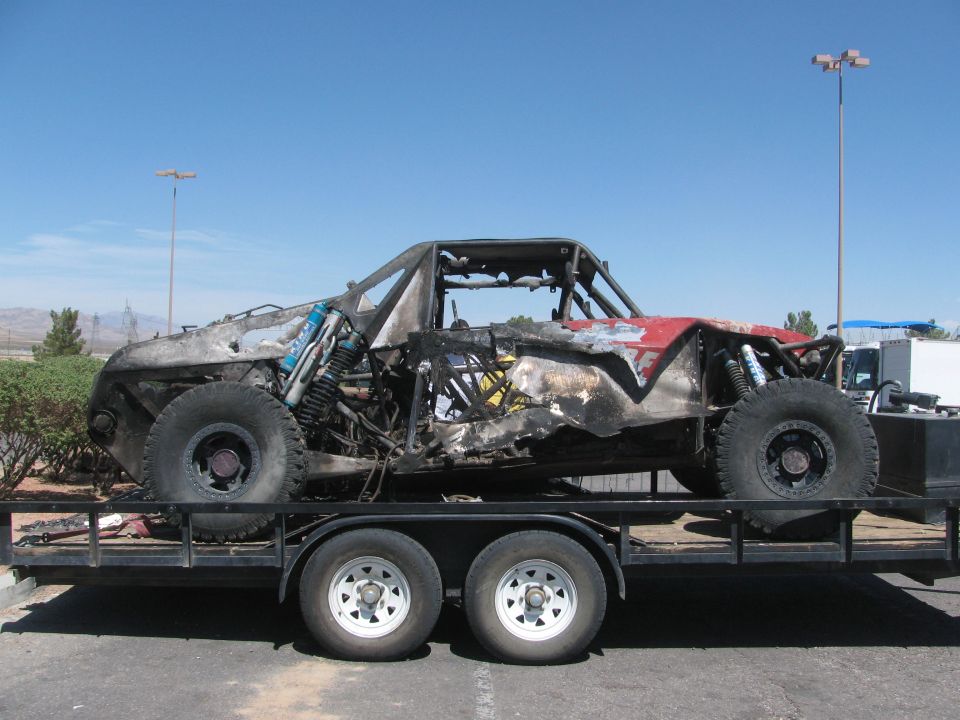 Side view of a burned tube-frame off-road race car on a flatbed trailer