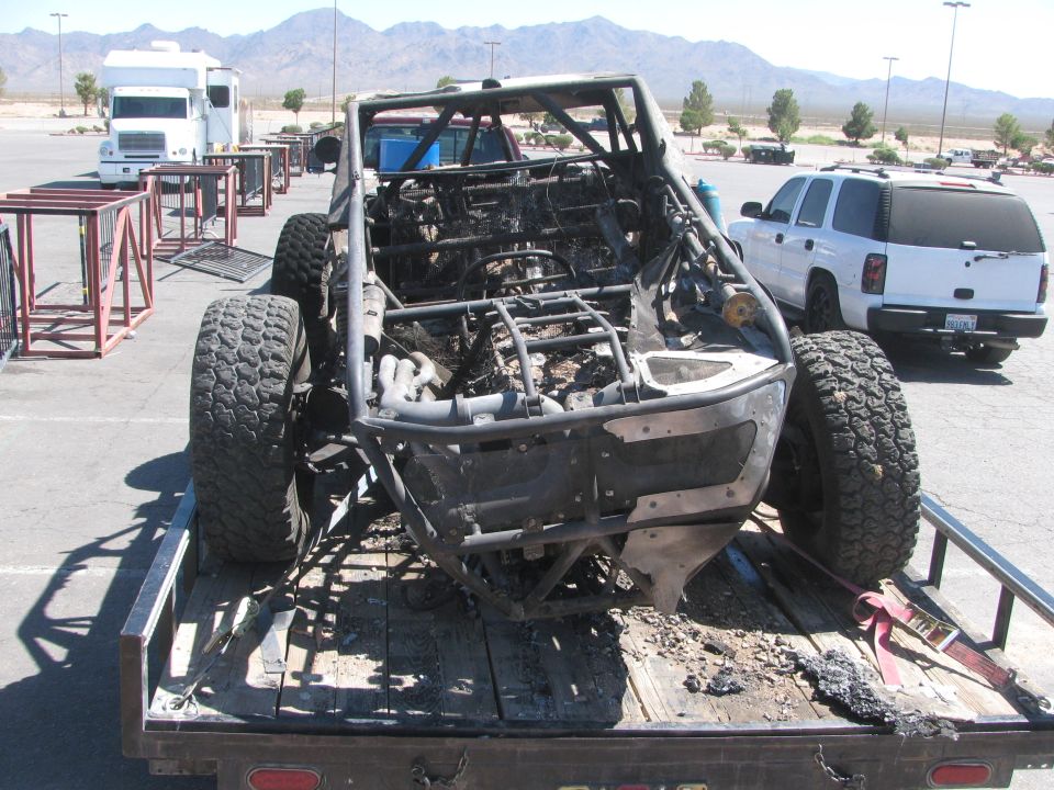 Rear view of a burned-out off-road race car frame on a flatbed trailer