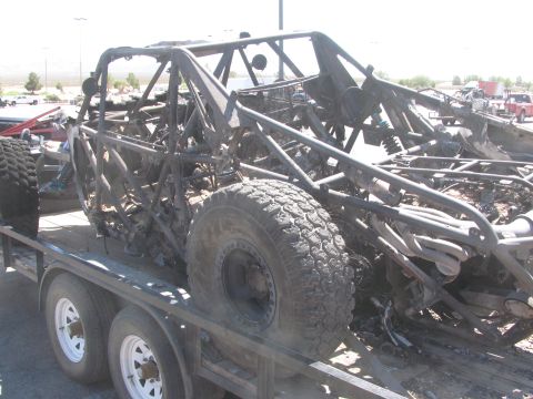 1990 Ford Bronco - heavily burned tube-frame off-road race car sits on a flatbed trailer, its bodywork gone and chassis blackened by fire.