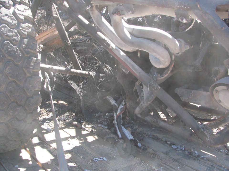 Close-up of charred exhaust headers and suspension under a burned race car