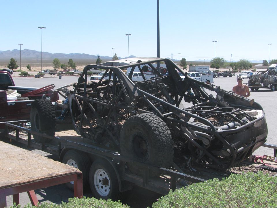 Burned-out off-road race car on flatbed trailer in desert parking lot