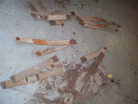 1969 Ford Torino - Multiple leaf springs, some broken, lie on a dusty concrete surface. The parts appear to be old and heavily rusted.