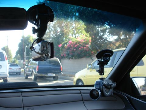 1993 Ford Taurus - View from inside a car shows two dashboard cameras attached to the windshield, with traffic visible through the glass.