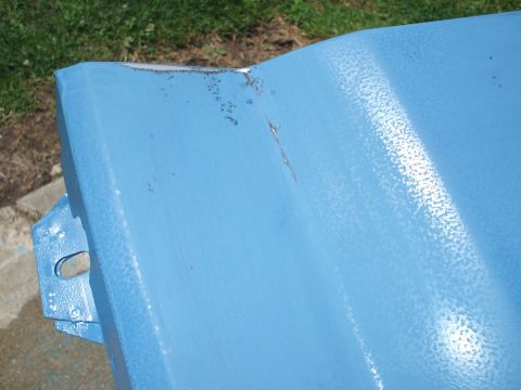 1990 Ford Bronco - A close-up view of a blue painted metal component, possibly a car part, showing signs of wear and tear.