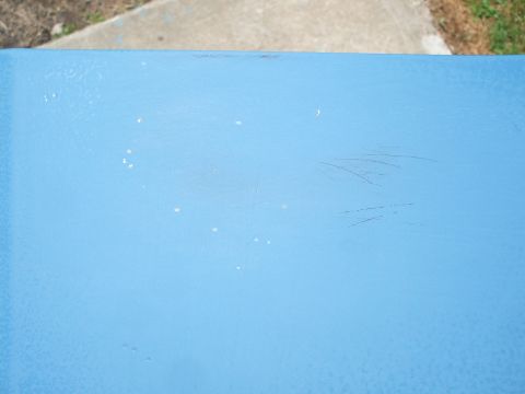 1990 Ford Bronco - Close-up of a blue painted surface showing scratches and white specks, with a watermark at the bottom right.