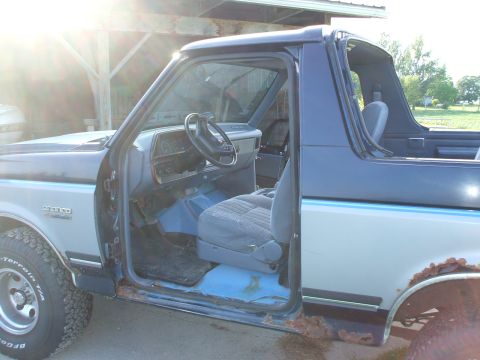 1990 Ford Bronco - The interior of a 1990 Ford Bronco is visible with the driver's door open, revealing the seats and dashboard.