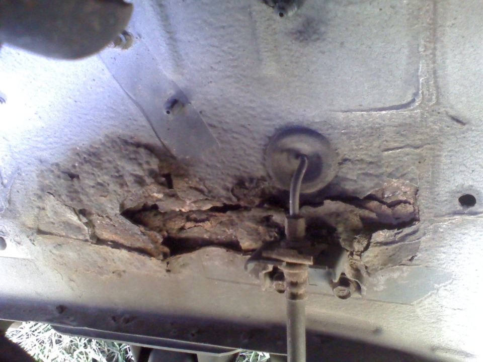 Heavily rusted section of a vehicle's undercarriage with a brake line visible