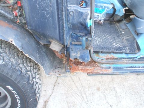 1990 Ford Bronco - Significant rust damage is visible on the door sill and fender of this blue vehicle, with a BFGoodrich tire in the foreground.