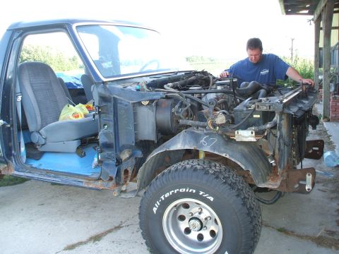 1990 Ford Bronco - A man works on the engine of a disassembled Ford truck, revealing its internal components and frame.