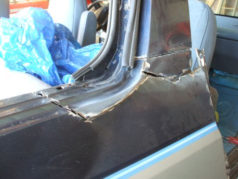 1990 Ford Bronco - Close-up of a damaged vehicle door frame and interior, with a blue tarp covering the seats.