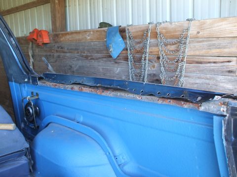 1990 Ford Bronco - The interior of a blue vehicle shows signs of rust and wear, with a wooden wall and chains in the background.
