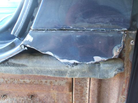 1990 Ford Bronco - Close-up of a damaged blue car panel showing rust and wear on the underlying metal.