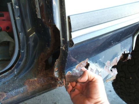 1990 Ford Bronco - Severe rust damage is visible on the door frame and rocker panel of a vehicle.