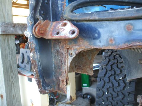 1990 Ford Bronco - Close-up of severe rust damage on a vehicle's door hinge and surrounding body panels.
