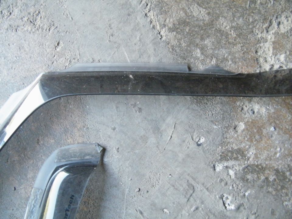 Black car fender section with chrome trim and part of a black plastic trim piece. Text on plastic trim is illegible