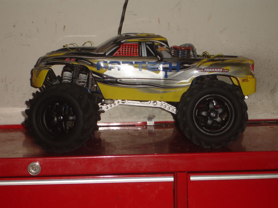 Yellow and silver remote control monster truck with large tires and racing decals, side view