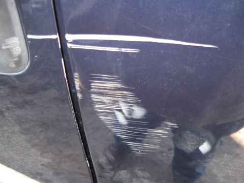 2005 Ford F-150 - The door of a dark blue vehicle shows significant damage from scratches and scuffs.