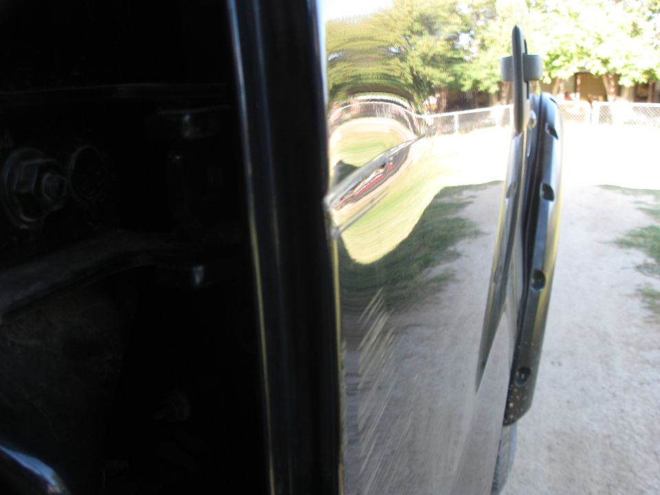 Close-up of a black truck door hinge and part of the door panel. Scratches are visible on the door