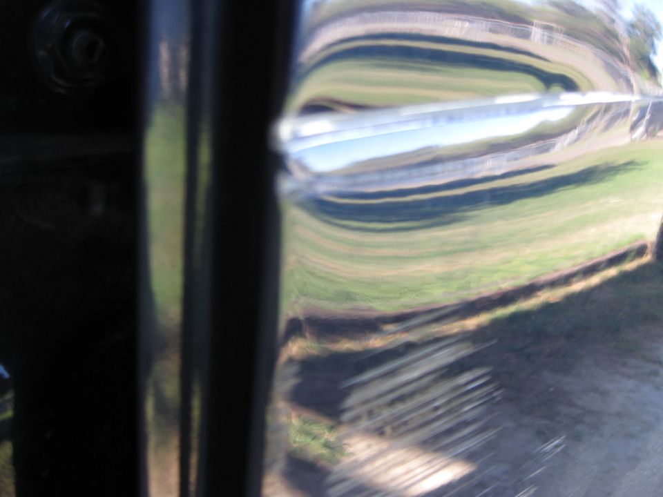 Black truck door with chrome handle, reflecting a grassy field and sky