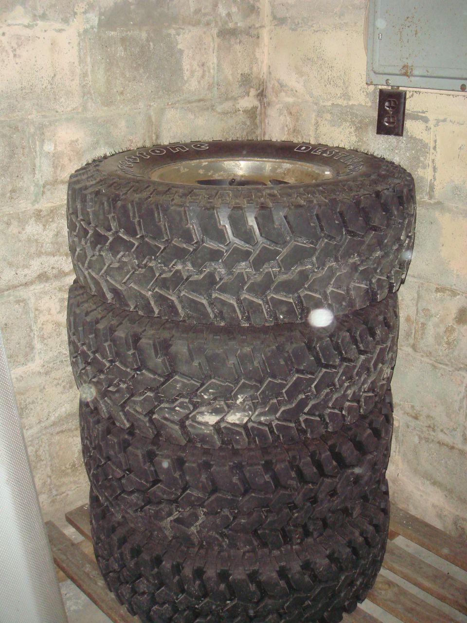 Stack of four off-road tires with visible tread pattern and sidewall text