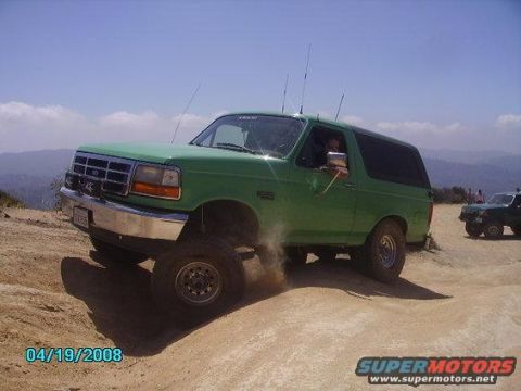 1996 Ford Bronco - A green 1996 Ford Bronco navigates a dusty off-road trail with another vehicle in the distance.