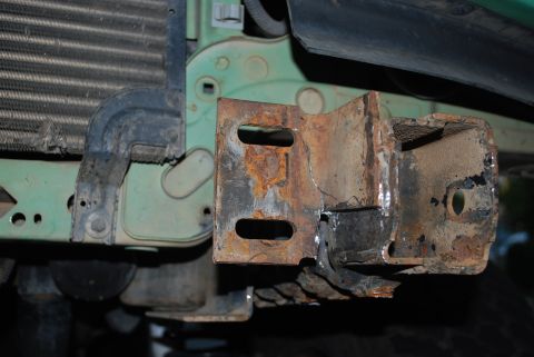 1996 Ford Bronco - Close-up view of a corroded bracket and radiator assembly on a vehicle's front end.