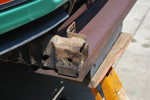 1996 Ford Bronco - Close-up of a rusted metal frame part being worked on, supported by wooden blocks and a jack stand.