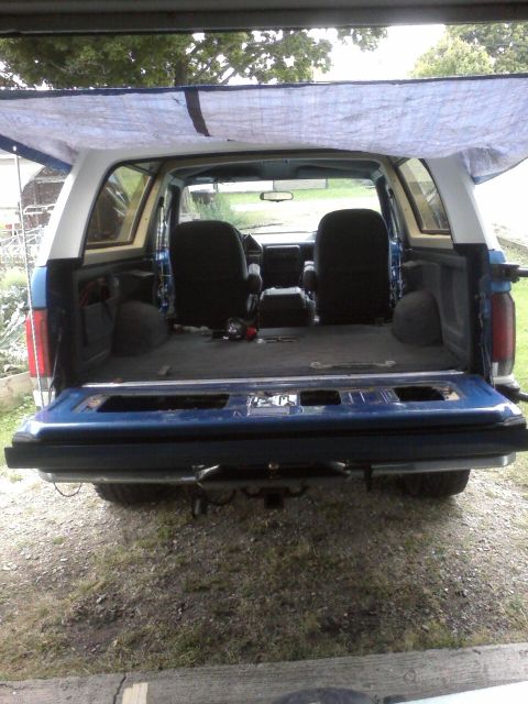 1991 Ford Bronco - Rear view of a blue and white Ford Bronco, with its tailgate down and a tarp overhead.