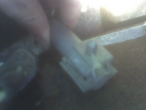 1991 Ford Bronco - A hand is shown holding a white electrical connector with several pins, likely part of a vehicle's wiring harness.