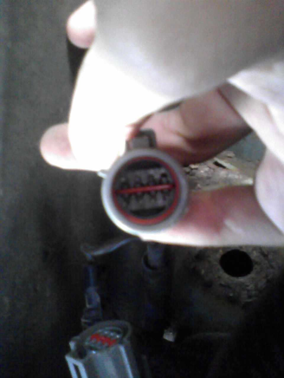 Close-up of a gray electrical connector with red trim and visible pins, held by a hand