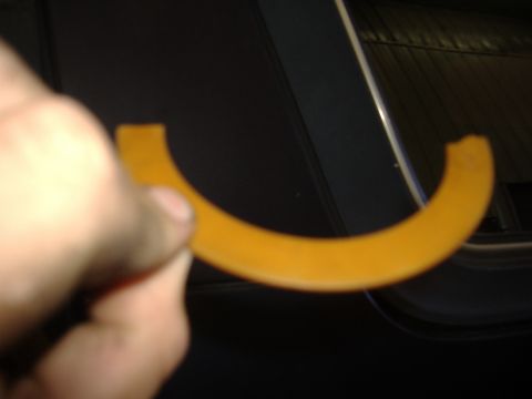1988 Ford Bronco - A hand holds up a horseshoe-shaped orange-yellow polyurethane bushing or spacer ring in front of a dark vehicle body panel. The C-shaped pa…