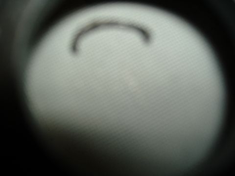 1988 Ford Bronco - Heavily out-of-focus close-up of a small broken C-shaped metal snap ring or clip lying on a pale textured surface, framed by dark blurred e…