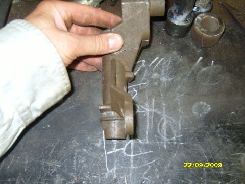 1989 Ford Bronco - A cracked metal component is held by a hand over a workbench with chalk markings and a date stamp.