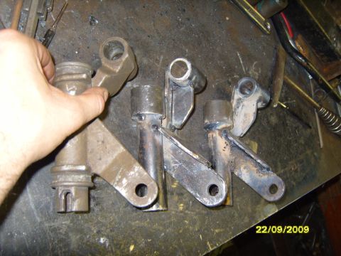 1989 Ford Bronco - Several metal brackets and parts are laid out on a workbench, with a hand holding one of them.